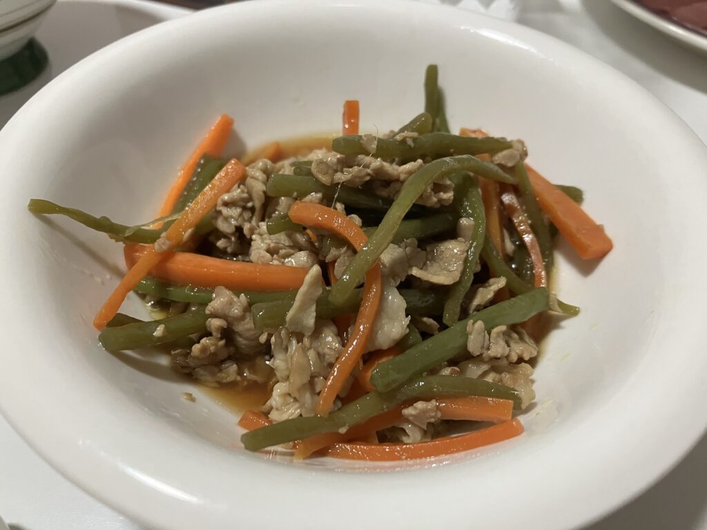 緑の野菜と人参、豚肉の入った和風の炒め物が白い皿に盛られている