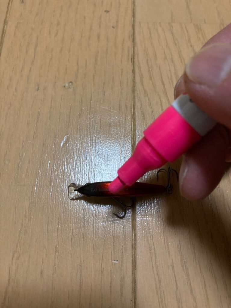 ピンクのマーカーでルアーに色を塗っている手。