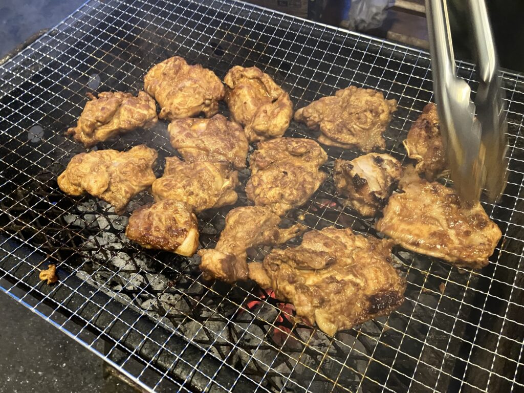 炭火で焼かれた肉の塊が網の上に並んでいるバーベキューのシーン