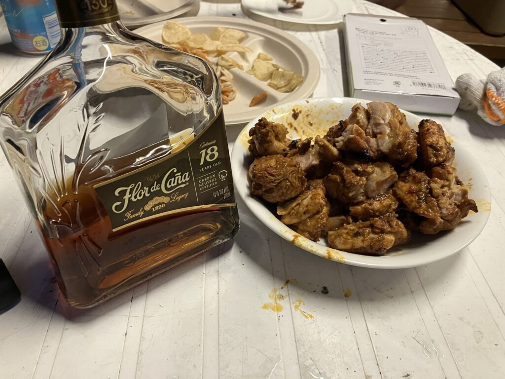 テーブルの上に置かれたボトルと、鶏肉が盛られた皿。ボトルは"Flor de Caña"というラム酒で、鶏肉はスパイシーなマーリネが施されている。