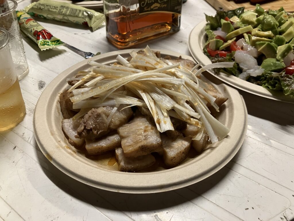 盛り付けられた豚の角煮にネギの千切りが添えられた皿と、新鮮なサラダが並んでいるテーブルの上の様子