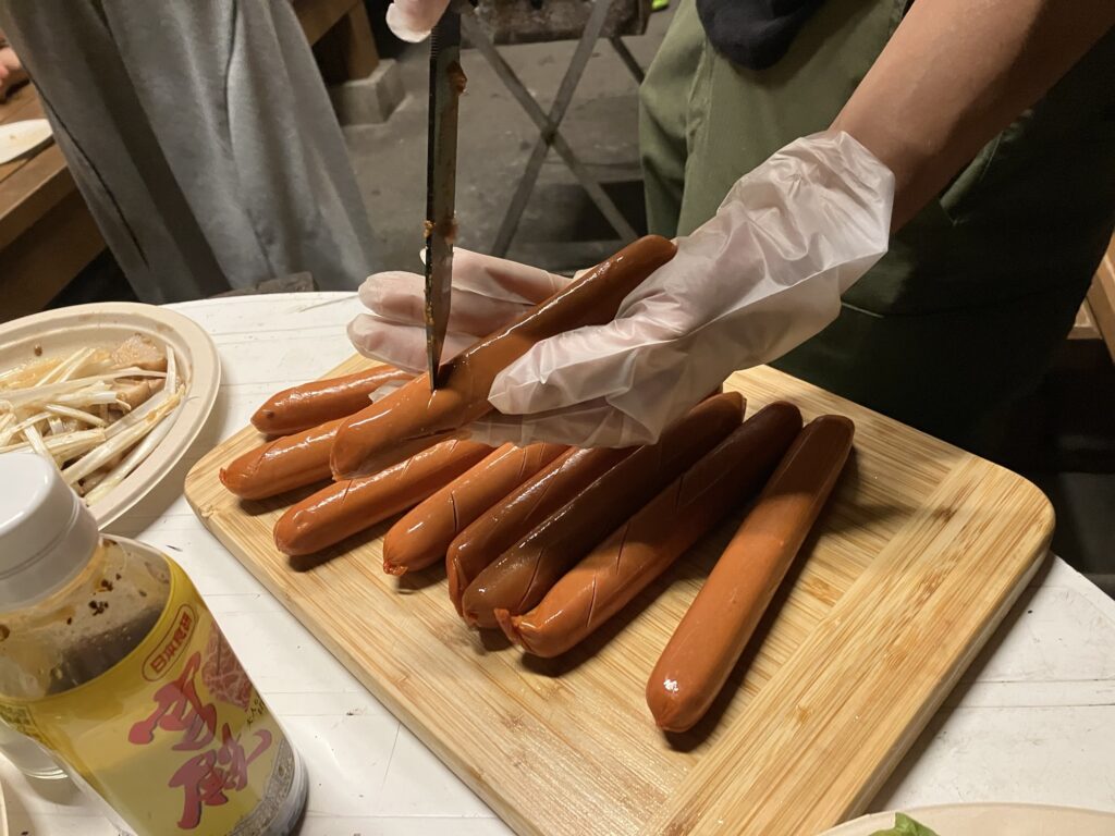 BBQの準備中、ハンドグローブをつけた手でソーセージを切っている様子。