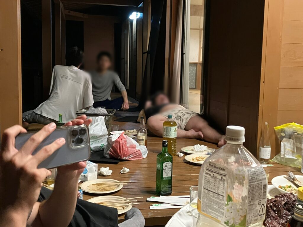 BBQを楽しむ会社のメンバーたちが集まる様子。テーブルには食事と飲み物が並び、リラックスした雰囲気の中で談笑している。