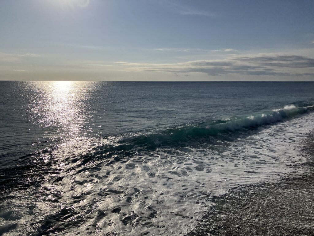 海の景色と波が光を反射している朝の風景。日が昇り、静かな海面に波が寄せている.